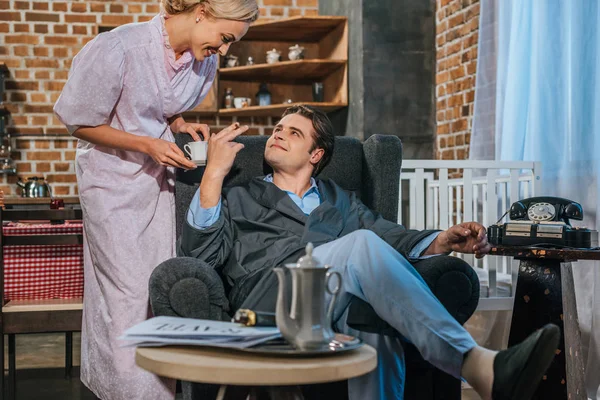 Uomo sorridente in accappatoio fumare sigaretta e guardando felice moglie in possesso di una tazza di caffè, stile 1950 — Foto stock