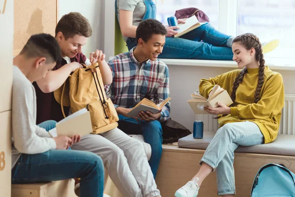 Lächelnde multikulturelle Gymnasiasten, die in der Schulpause Bücher lesen und reden — Stockfoto