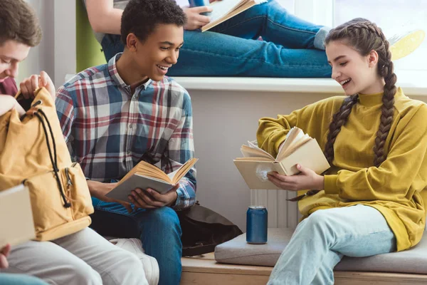 Escolares multiétnicos sonrientes leyendo libros durante las vacaciones escolares - foto de stock