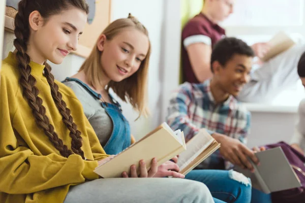 Groupe d'adolescents multiculturels souriants lisant des livres pendant les vacances scolaires — Photo de stock