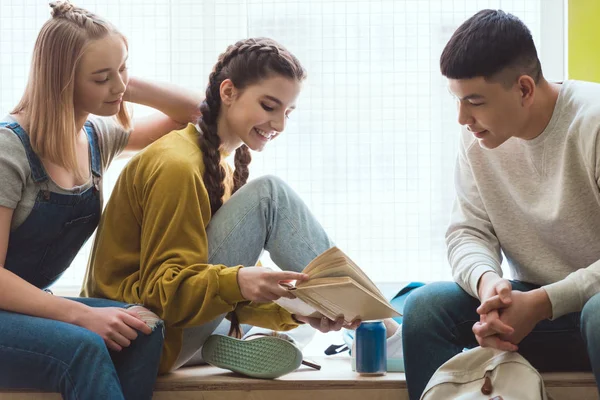 Smiling high school female student showing book to classmates during school break — Stock Photo