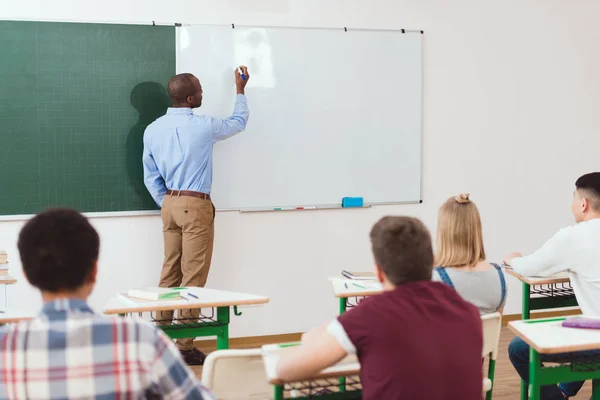 Задний вид старшеклассников и учителей, пишущих на белой доске в классе — стоковое фото