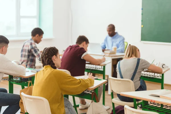 Vista trasera de la escritura de los alumnos de secundaria y la escritura afroamericana en el ordenador portátil - foto de stock