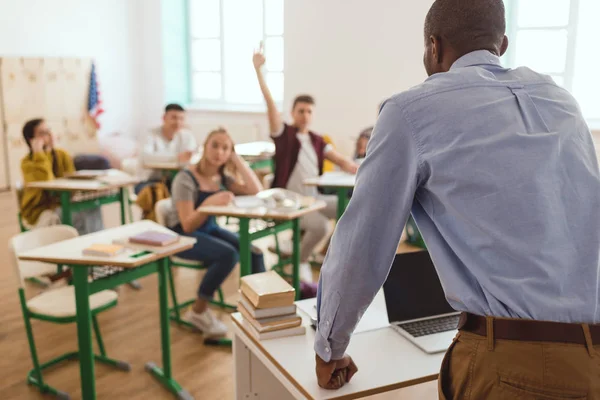 Rear view of african american teacher and schoolboy with arm up in classroom — Stock Photo