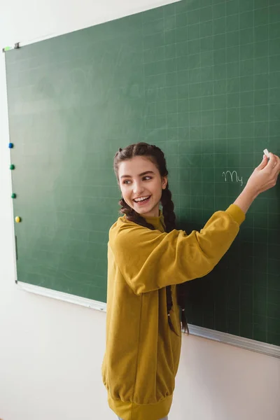 Smiling high school female student writing on chalk board — Stock Photo