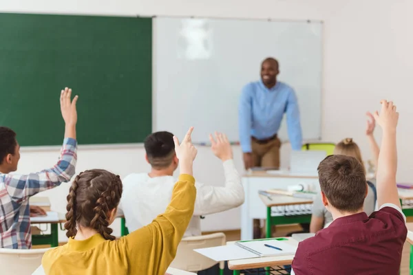 Rückansicht von Gymnasiasten mit erhobenen Armen und afrikanisch-amerikanischem Lehrer im Klassenzimmer — Stockfoto