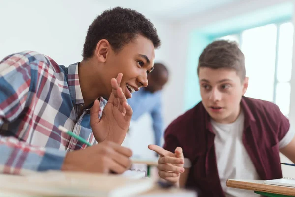 Smiling multicultural high school teenage students talking during lesson and teacher standing behind in classroom — Stock Photo