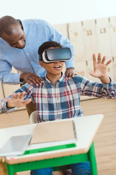 Professeur afro-américain tenant les épaules d'un écolier en utilisant un casque de réalité virtuelle — Photo de stock