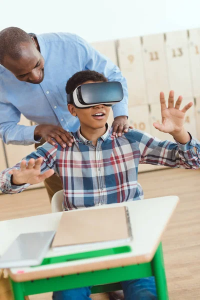 Africano professor americano segurando ombros de estudante usando fone de ouvido realidade virtual — Fotografia de Stock