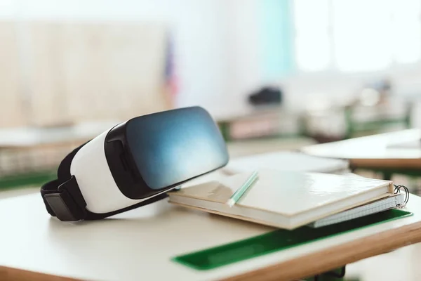 Closeup shot of virtual reality headset on table with textbook and pencil in classroom — Stock Photo