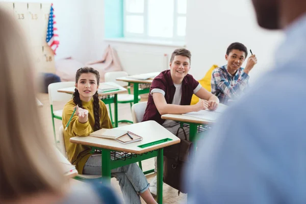 Image recadrée de l'enseignant avec écolière et camarades de classe assis à des bureaux — Photo de stock