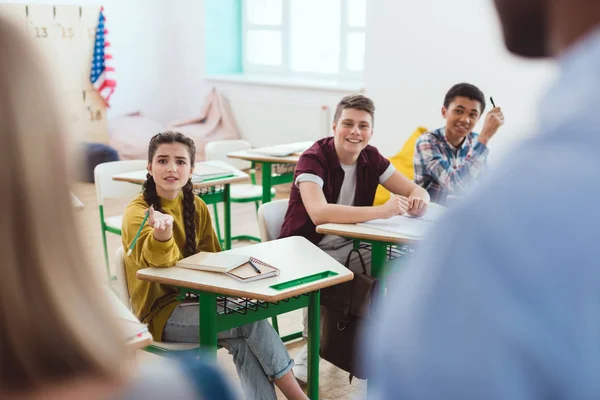 Imagen recortada del profesor con la colegiala y compañeros de clase sentados en escritorios - foto de stock