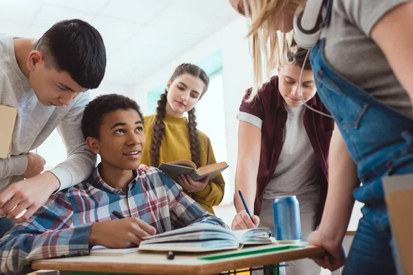 Estudiantes de secundaria ayudando a su compañero de clase con la tarea en la escuela - foto de stock