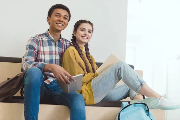 Feliz pareja de estudiantes de secundaria haciendo deberes en el pasillo de la escuela juntos - foto de stock