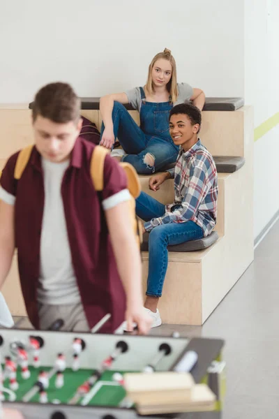 Adolescentes estudiantes pareja pasar tiempo juntos en el pasillo de la escuela y mirando juego de patadas - foto de stock