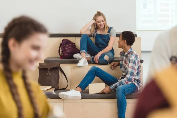 Adolescentes estudiantes pareja sentado en la escuela pasillo - foto de stock