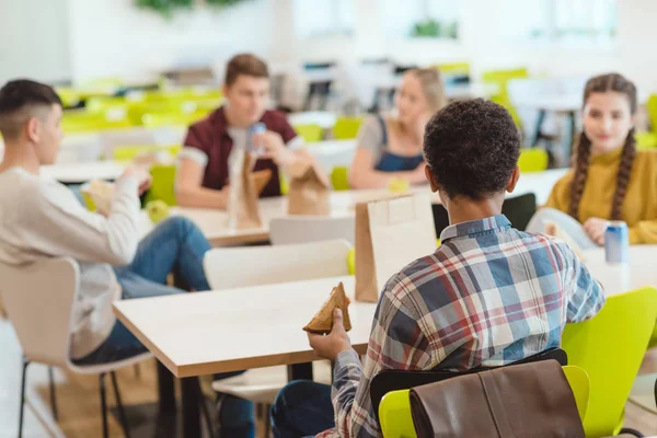 Grupo de estudiantes adolescentes charlando mientras almuerzan en la cafetería de la escuela - foto de stock