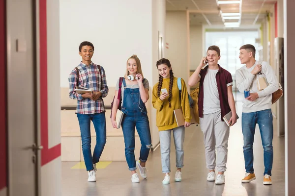 Happy high school classmates walking by school corridor together — Stock Photo