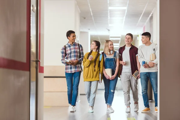 Groupe de camarades de classe souriants du secondaire marchant ensemble par couloir scolaire — Photo de stock