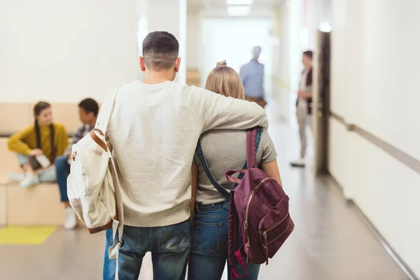 Visão traseira de estudantes adolescentes casal andando pelo corredor da escola e abraçando — Fotografia de Stock