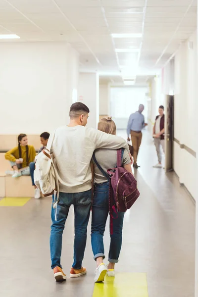 Rear view of teenage students couple walking by school corridor and embracing — Stock Photo