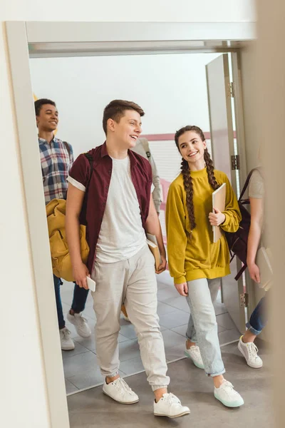 Grupo multiétnico de estudiantes de secundaria caminando por el pasillo de la escuela en el descanso — Stock Photo