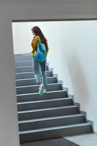 Rear view of schoolgirl with backpack walking upstairs — Stock Photo