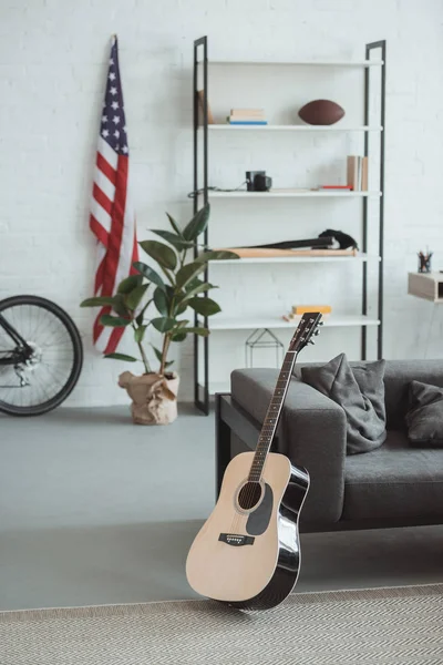 Interior de la sala de estar moderna con bandera americana, estantes, maceta, guitarra y sillón - foto de stock