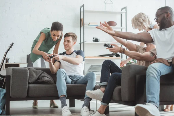 Young man showing joystick to african american woman and group of multicultural people pointing by hands — Stock Photo