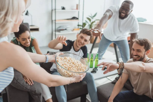 Immagine ritagliata di giovane donna che dà ciotola di popcorn a sorridenti amici multiculturali — Foto stock