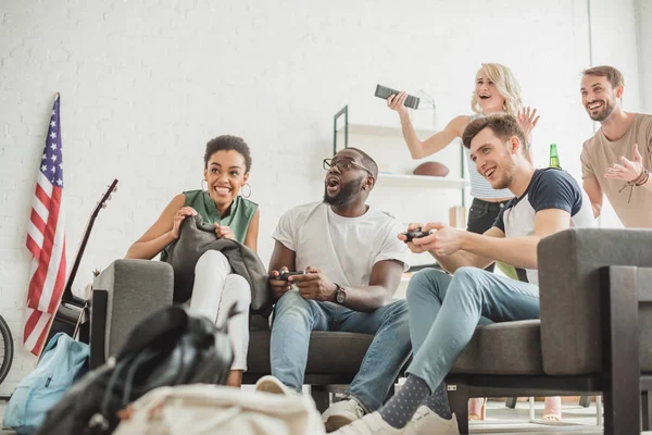 Faible angle de vue de heureux amis multiethniques avec joysticks jouer à un jeu vidéo — Photo de stock