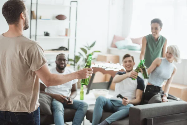 Вид ззаду молодого чоловіка з пляшкою пива в руках розмовляє з багатоетнічними друзями — стокове фото