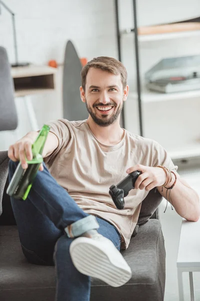 Joven sonriente sentado con botella de cerveza y joystick - foto de stock