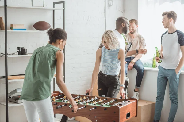 Mujeres jóvenes jugando al futbolín con amigos varones de pie detrás - foto de stock