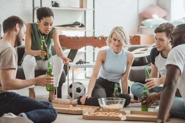 African american woman pointing by finger on pizza and group multicultural friends sitting near on floor — Stock Photo