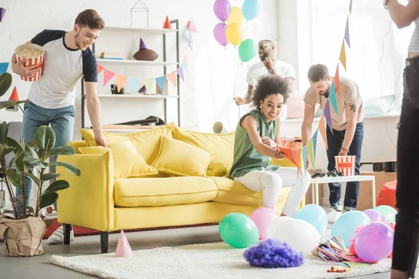 Jeunes amis multiculturels décorant salon avec ballons et guirlandes de fête — Photo de stock