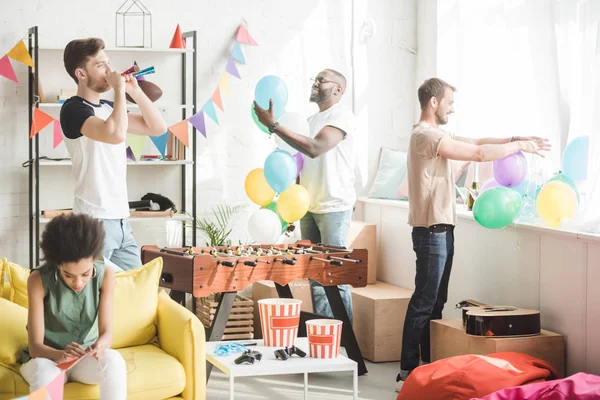 Afroamericano seduto sul divano con ghirlande da festa e giovani con corna da festa e palloncini — Foto stock