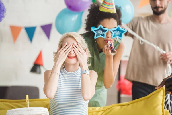 Joven hombre y mujer saludando chica rubia con pastel de cumpleaños en fiesta sorpresa - foto de stock