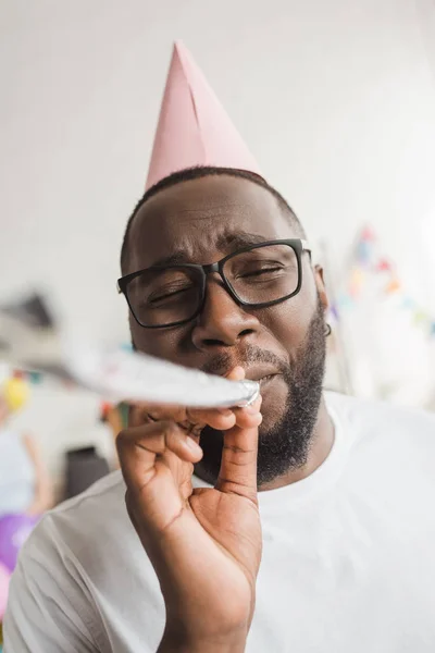 Feliz afro-americano em chapéu de festa soprando chifre de festa — Fotografia de Stock