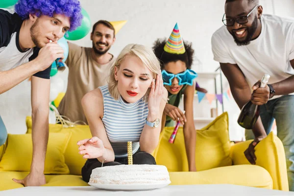 Blondine bläst Kerze auf Geburtstagstorte ihrer gut gelaunten Freunde — Stockfoto