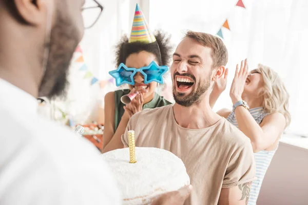 Amis multiraciaux saluant jeune homme avec gâteau d'anniversaire — Photo de stock