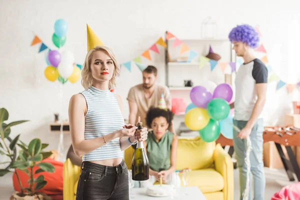 Blondes Mädchen mit Champagnerflasche vor feiernden Freunden — Stockfoto