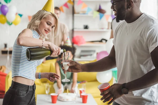 Mujer joven vertiendo champán en vidrio en manos de hombres afroamericanos - foto de stock