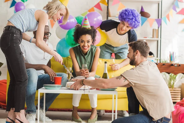 Giovani uomini e donne che tagliano la torta di compleanno a casa festa — Foto stock