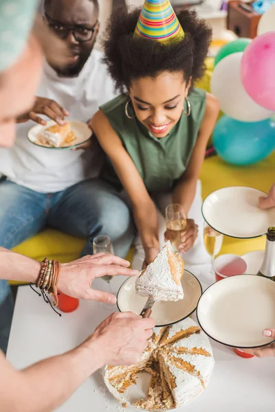 Hombres y mujeres jóvenes cortando pastel de cumpleaños en la fiesta - foto de stock