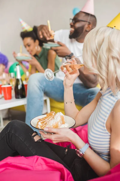 Attractive young woman holding plate with cake and drinking cocktail by her friends — Stock Photo