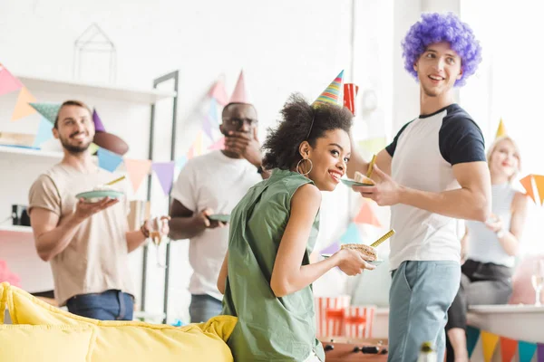 Young people in party hats celebrating birthday with drinks in cozy room — Stock Photo