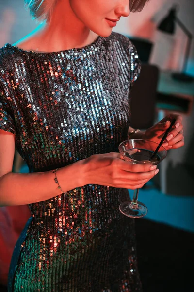 Vista de cerca de la chica en vestido de brillo celebración de vidrio con cóctel en la fiesta - foto de stock