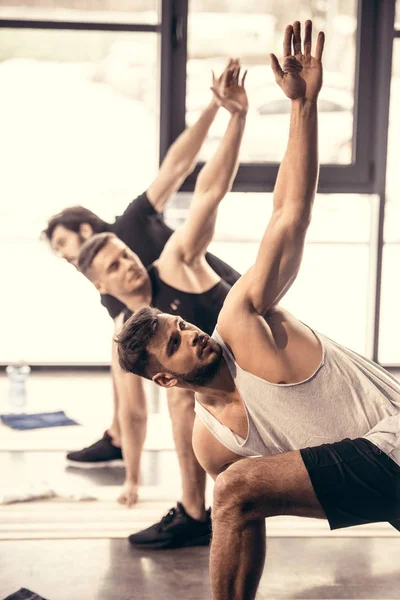 Handsome sportsmen simultaneously exercising and stretching in gym — Stock Photo