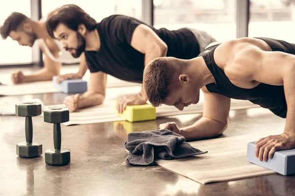 Beaux sportifs faisant simultanément de la planche et utilisant des blocs dans la salle de gym — Photo de stock